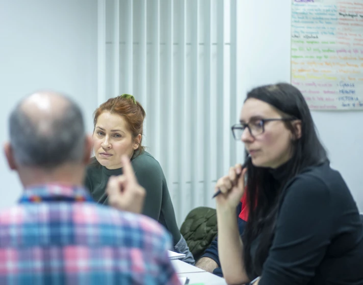 Lecturer leads a class discussion with students seated around a table and a population graph displayed behind. Lecturer leads a class discussion with students seated around a table and a population graph displayed behind.